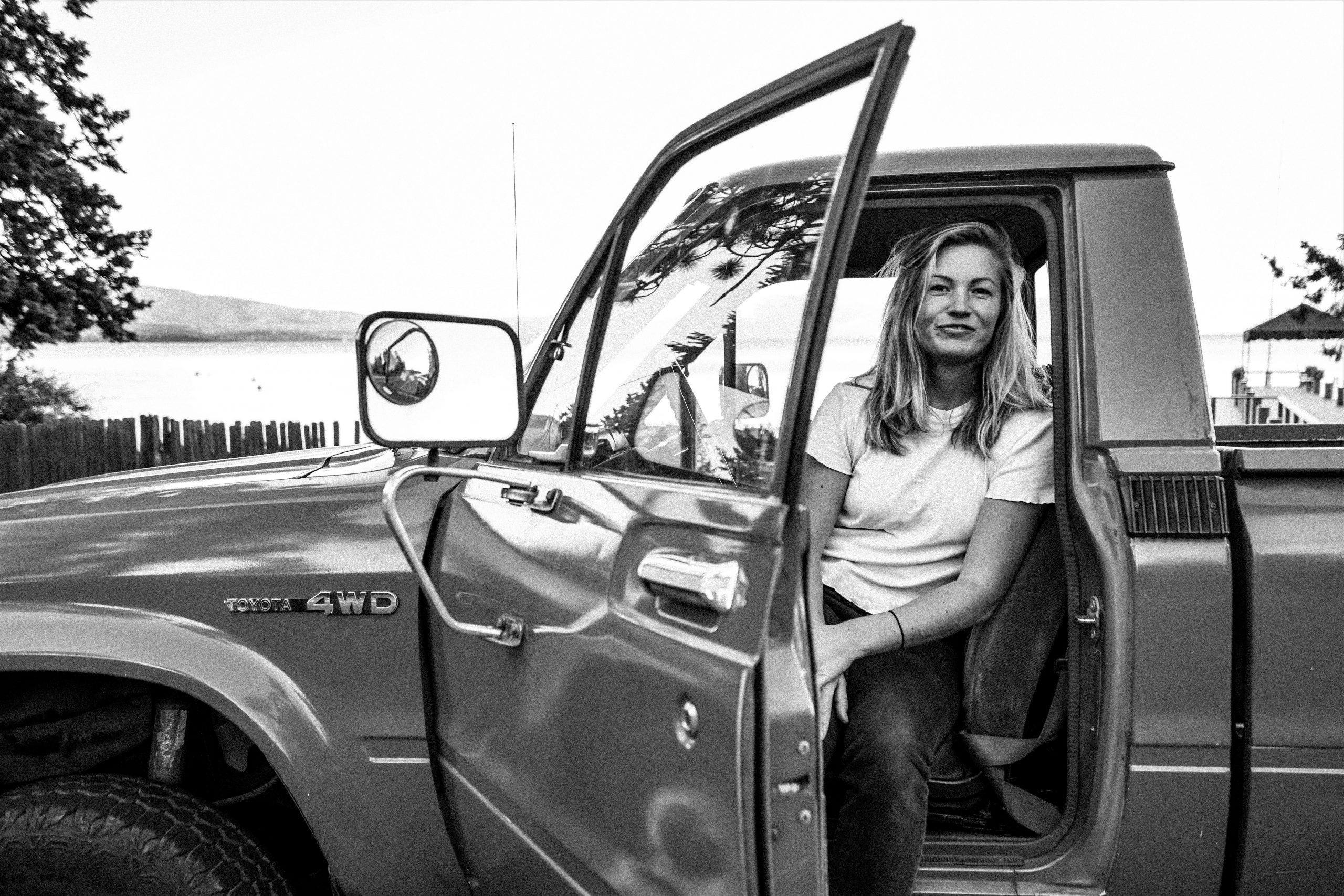 woman smiling at camera from front seat of vintage truck in black and white photo