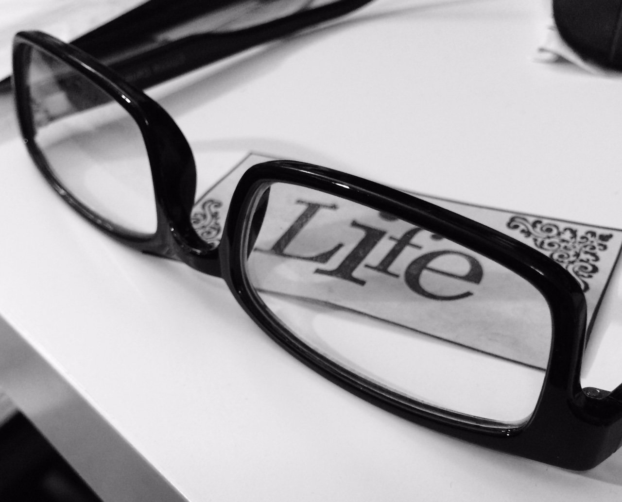 Black frame glasses around the word "Life" - black and white photo 